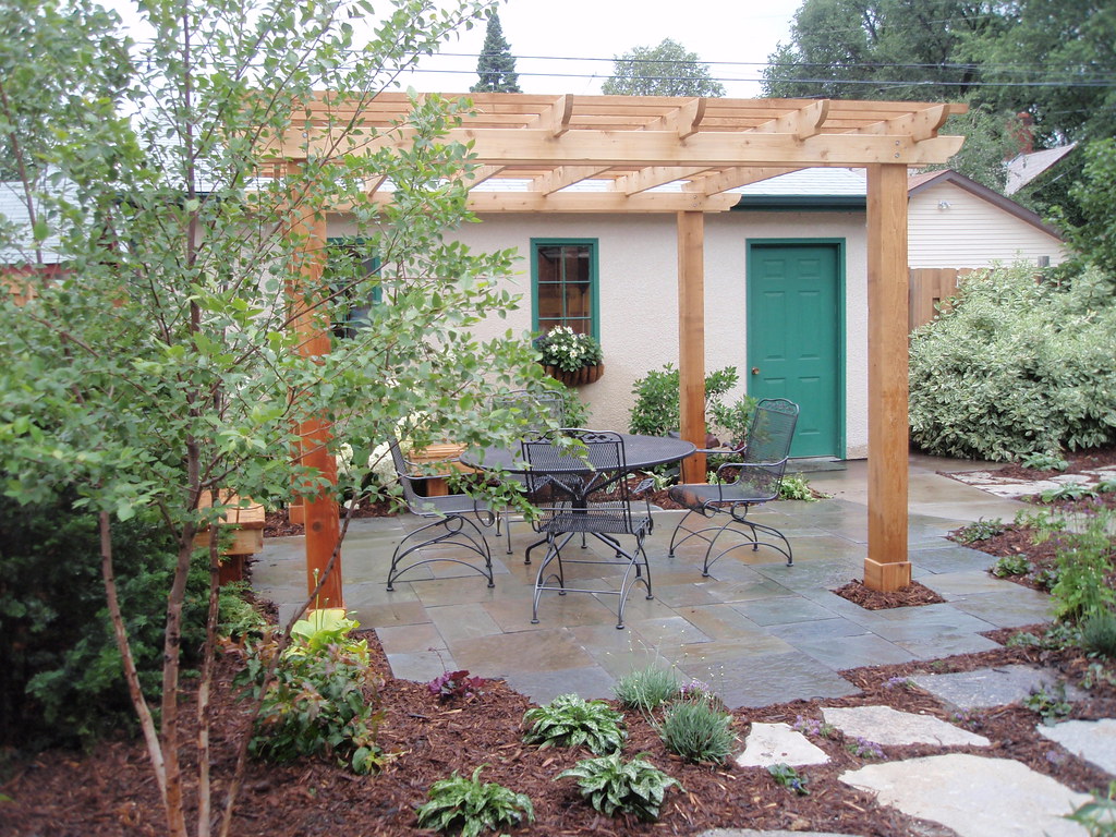 Timber pergola over a paved outdoor living area with garden beds